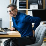 Osteopath for back pain Warrnambool visual: office worker seated, hand on lower back, depicting desk-related lumbar pain. ​