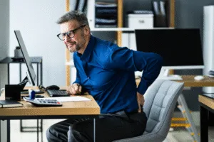Osteopath for back pain Warrnambool visual: office worker seated, hand on lower back, depicting desk-related lumbar pain. ​